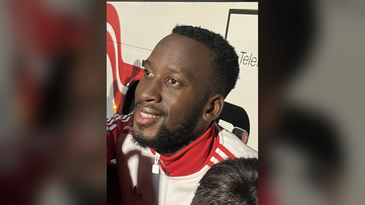 Dodi Lukébakio in a red and white Benfica training top, smiling beside the team bus